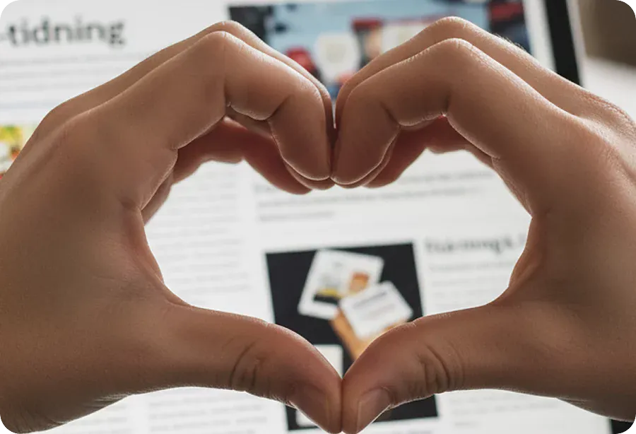 Händer som formar ett hjärta framför en surfplatta med en digital tidning på skärmen.
